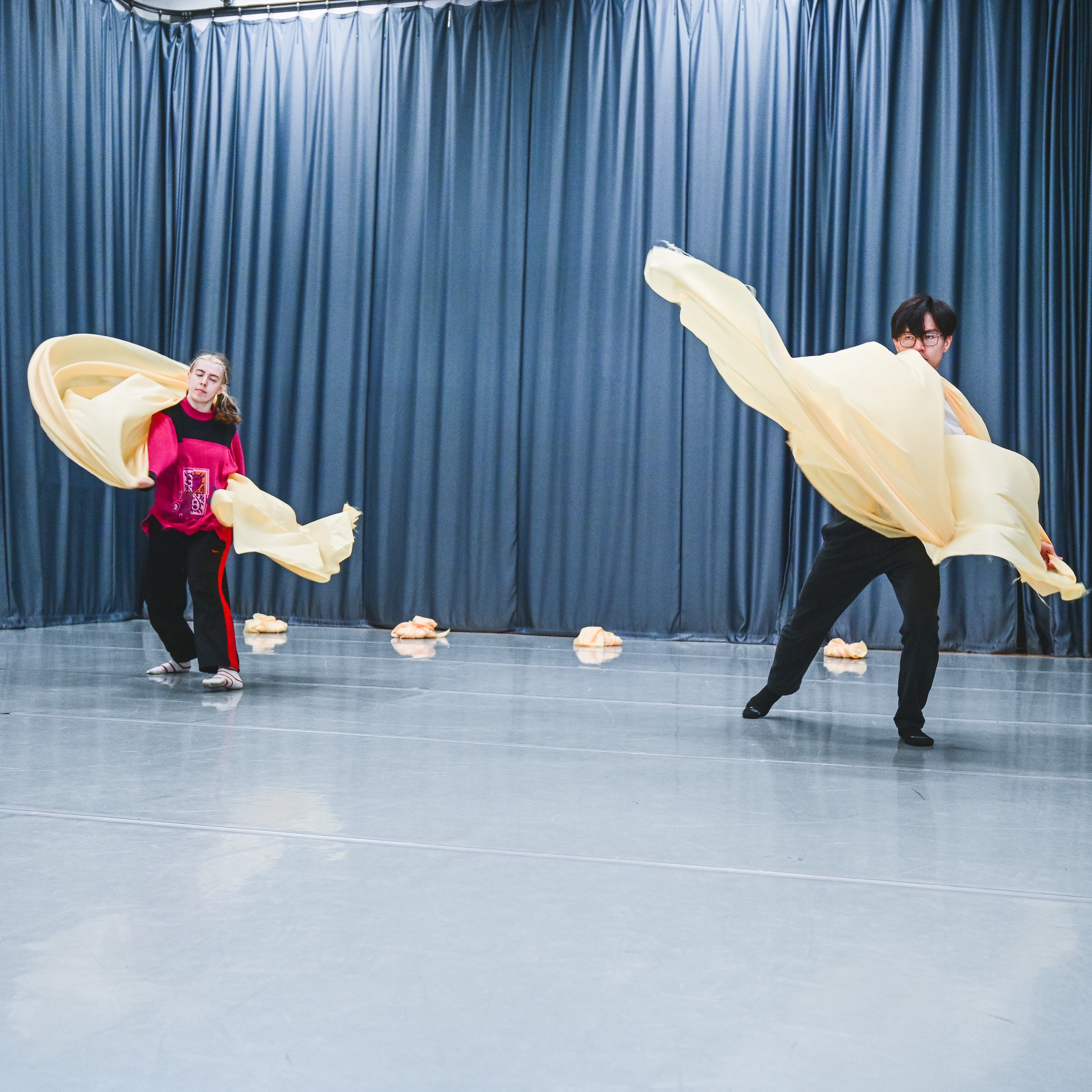 two dancers move with yellow fabric, throwing it outwards, the man gwyn studio has curtains around it shutting off the mirrors 