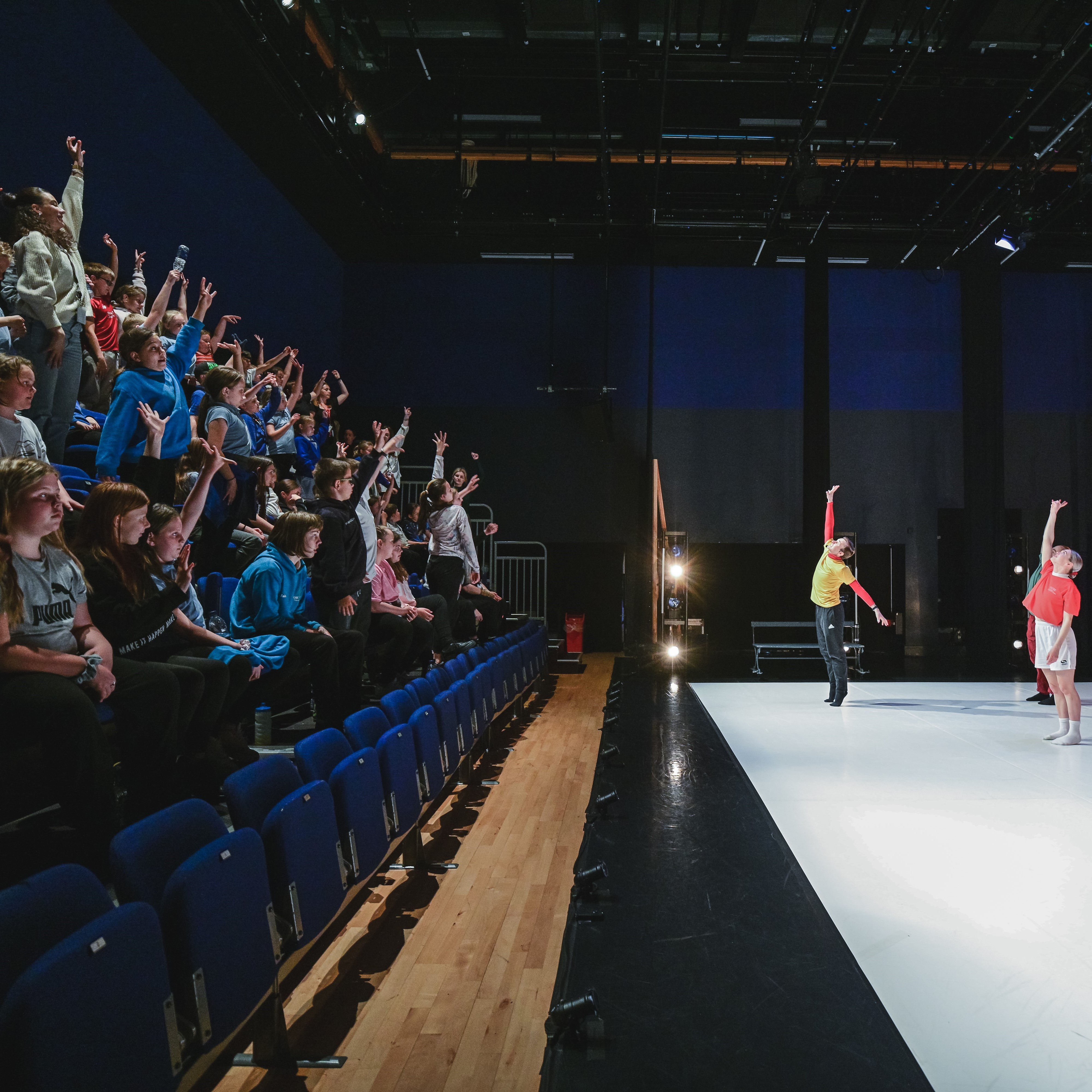 a performance for schools, children copy dancers from their seats - their arms in the air 