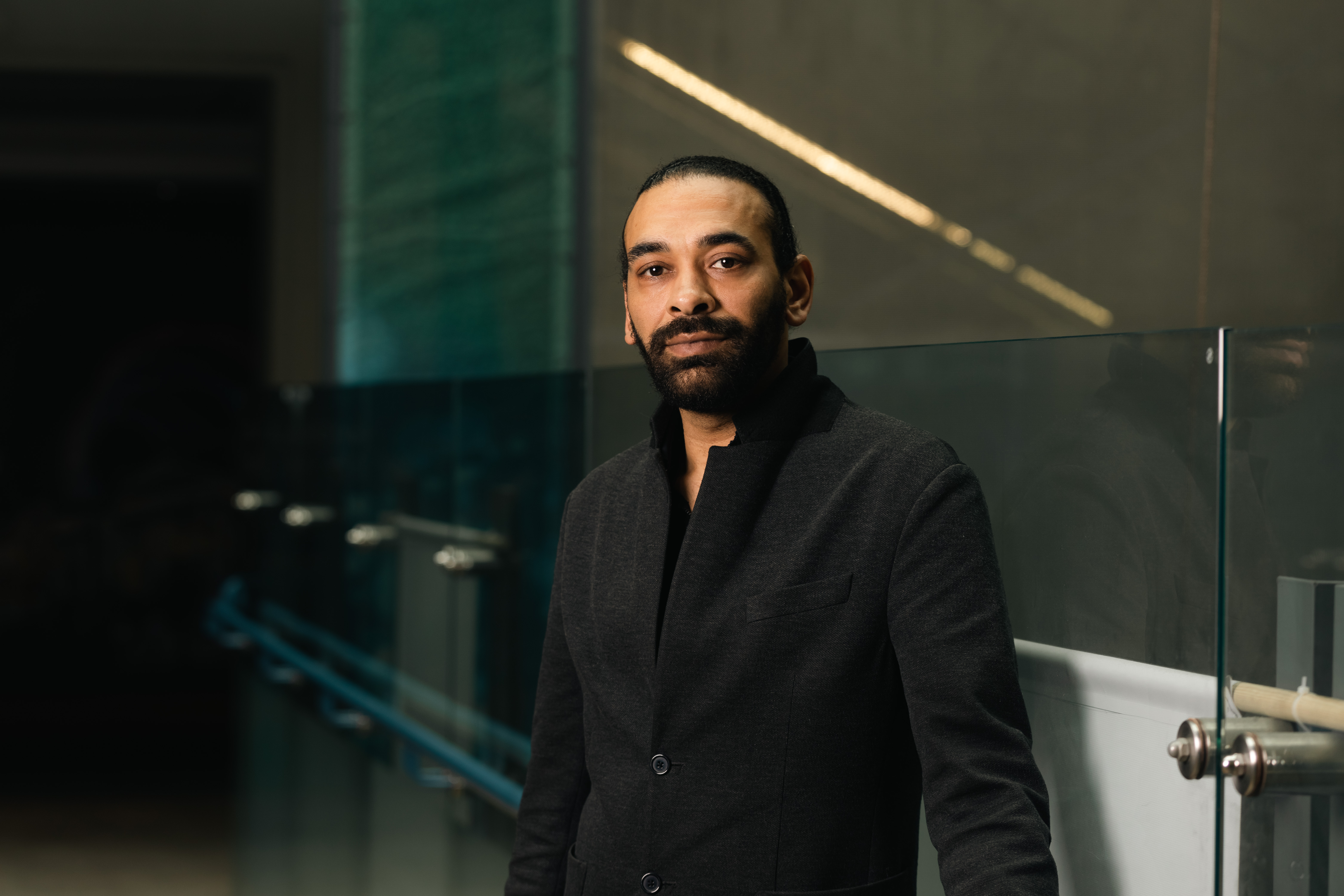 David Watson stands in a smart coat, he has short cropped hair and a neat black beard.