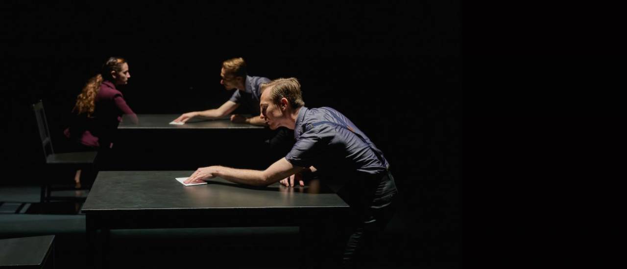 dancer pushing a piece of paper across a table towards a ghostly figure