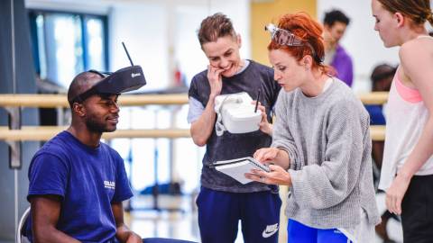 4 people looking at a notebook, 1 wearing a VR headset