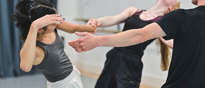 three dancers in rehearsals reaching towards one another whilst leaning backwards 