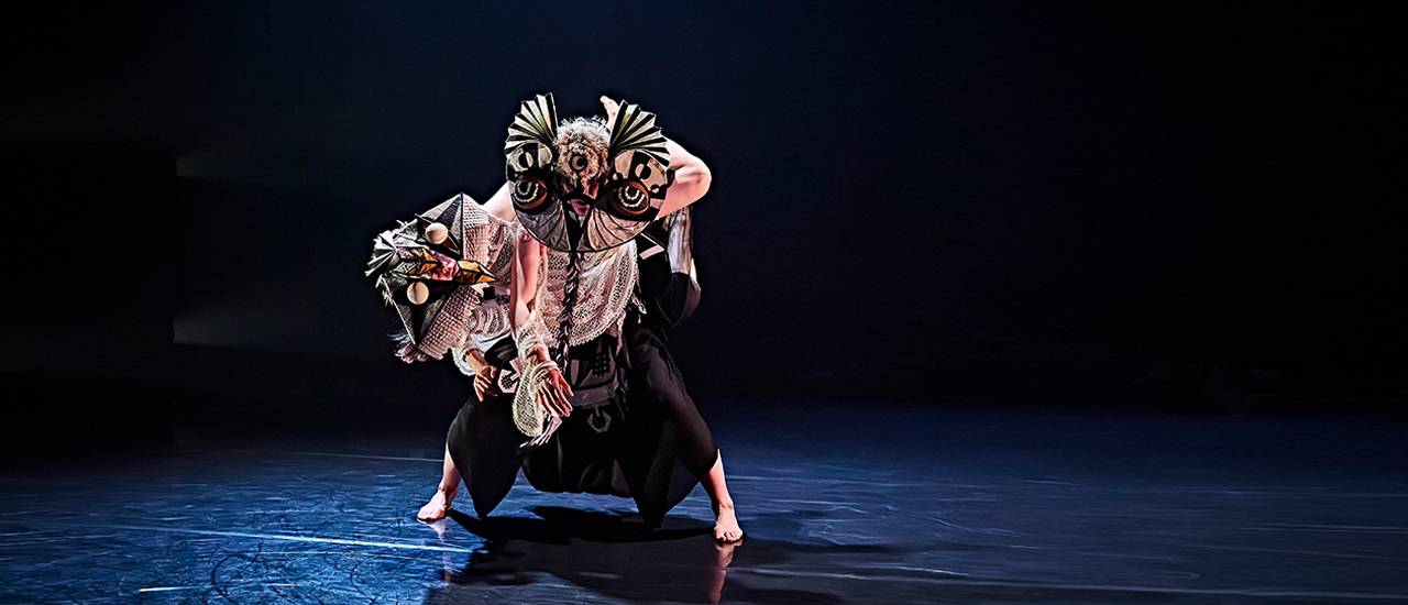 dancer in owl costume on black stage under dramatic blue lighting